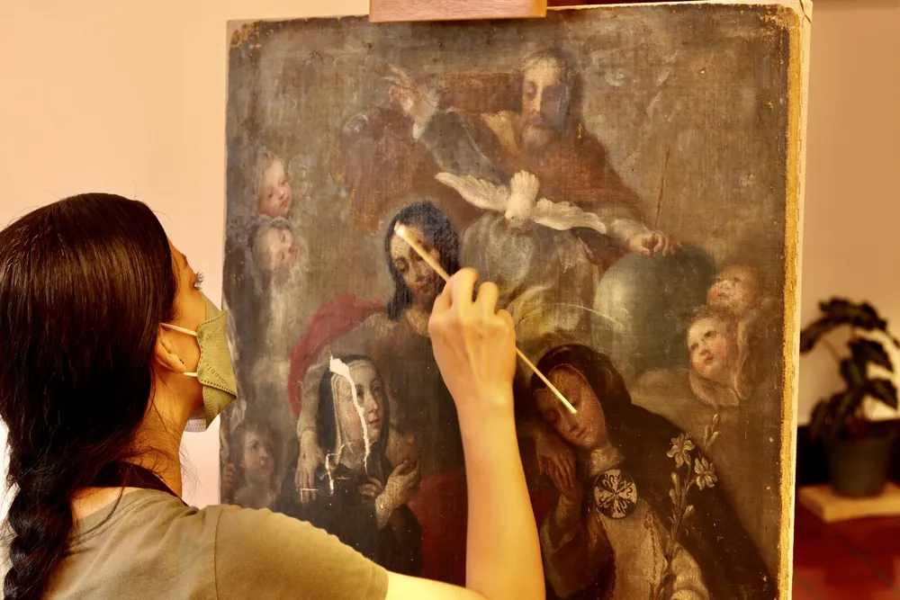 Restauradora realizando limpieza de una pintura de caballete virreinal sobre caballete en taller