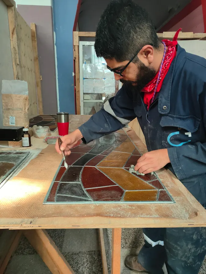 Restaurador trabajando en un vitral emplomado sobre mesa de taller